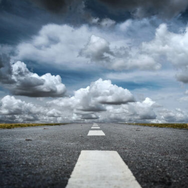 grey road leading to white fluffy clouds